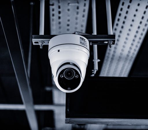 A monochrome image capturing the installation of a CCTV camera suspended from a ceiling.