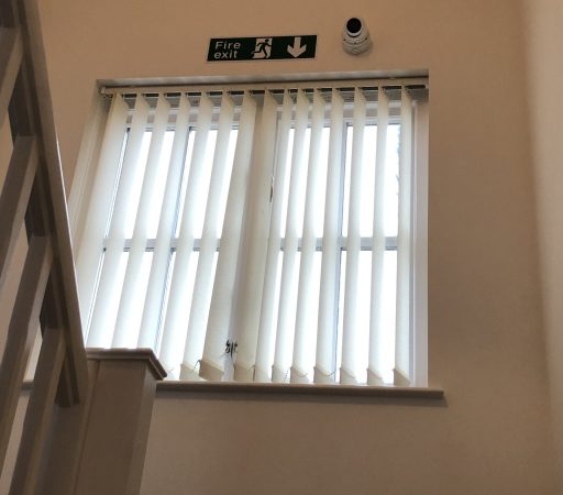 CCTV camera installed on a stairway with white blinds and a window.