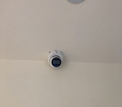 CCTV Camera installed on a white ceiling with a blue light on it.